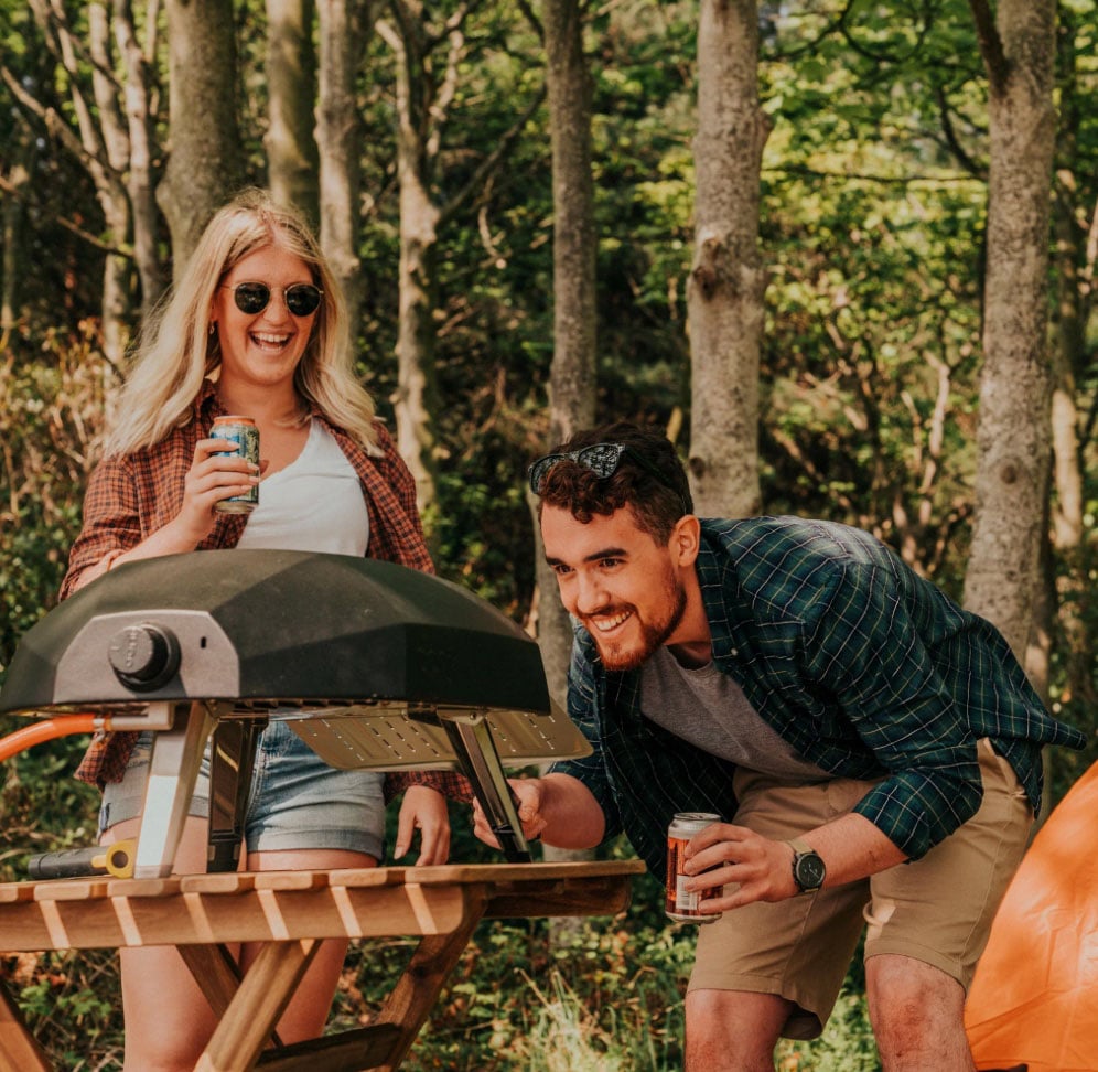 Man and woman using the Ooni Koda gas-powered outdoor pizza oven in a forest setting