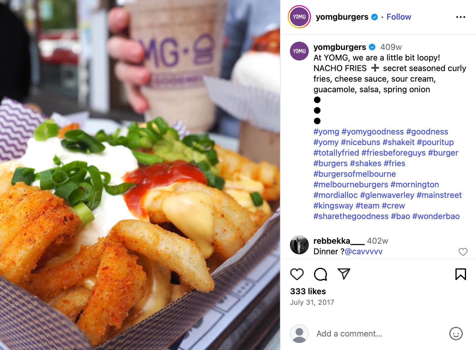 A tray of nacho fries topped with sour cream, cheese sauce, guacamole, salsa, and green onions, with a milkshake in the background